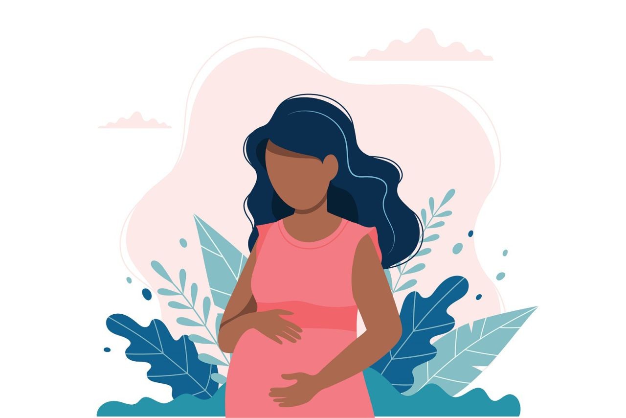 A pregnant woman with long black hair and brown skin wearing a pink dress holds her stomach